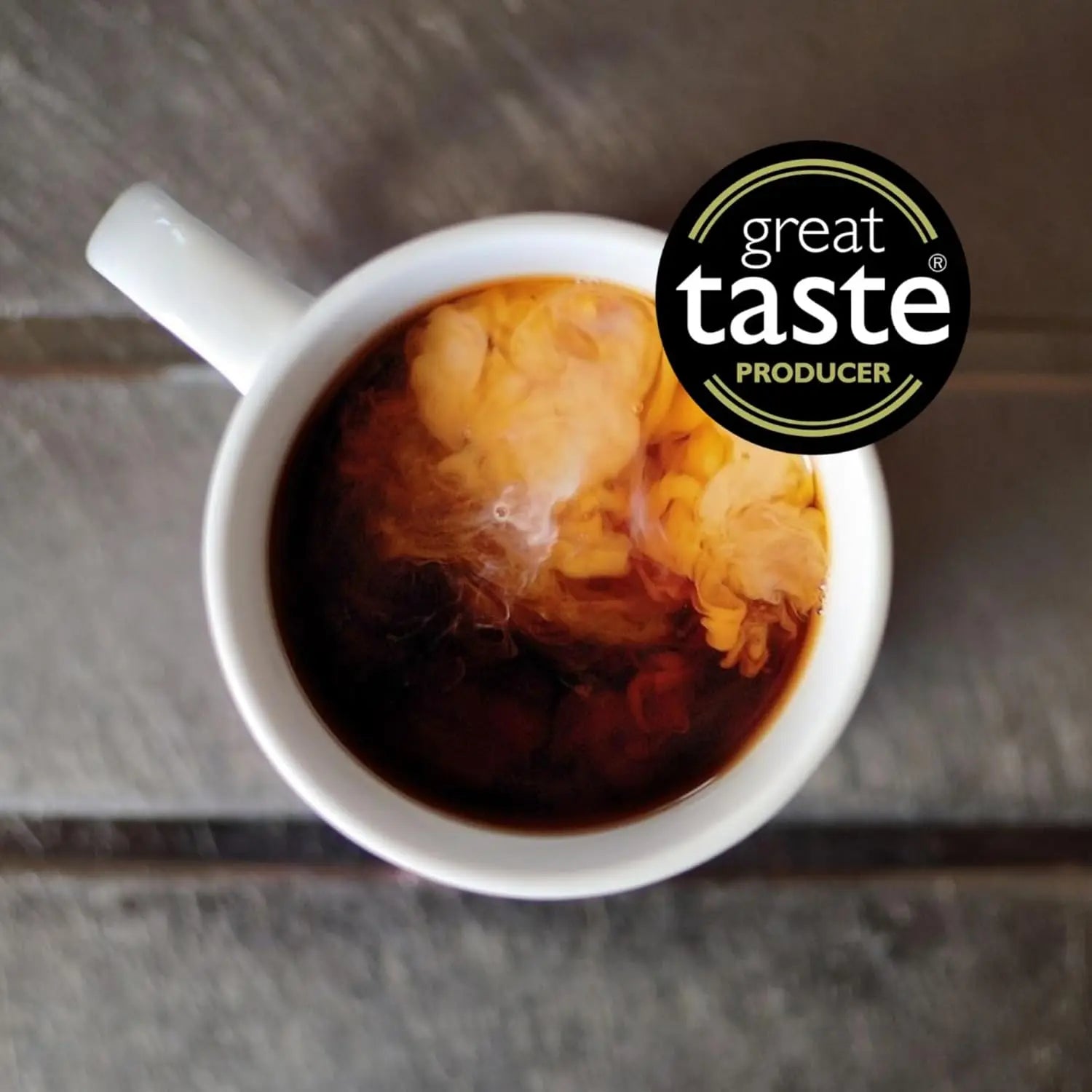 White mug with tea and a 'Great Taste Producer' logo on a wooden surface