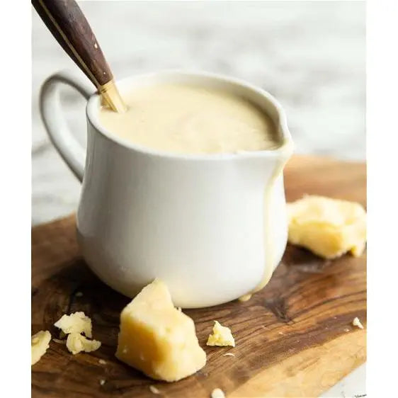 White pitcher filled with a creamy liquid on a wooden surface with chunks of cheese.
