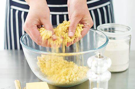Person preparing food with a bowl of yellow ingredients on a table.